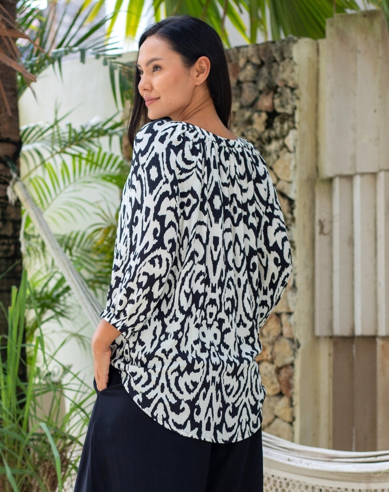 Woman wearing a black and white patterned top outdoors with greenery in the background