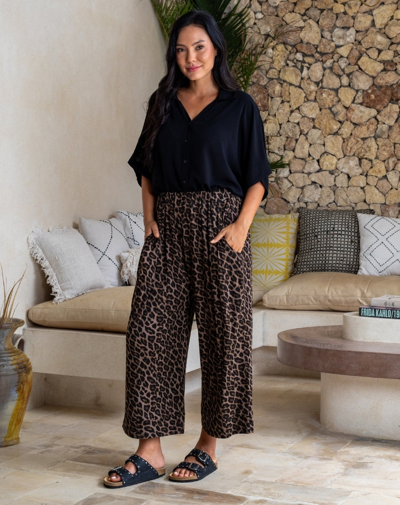 Woman wearing a black top and leopard print pants in a living room setting.