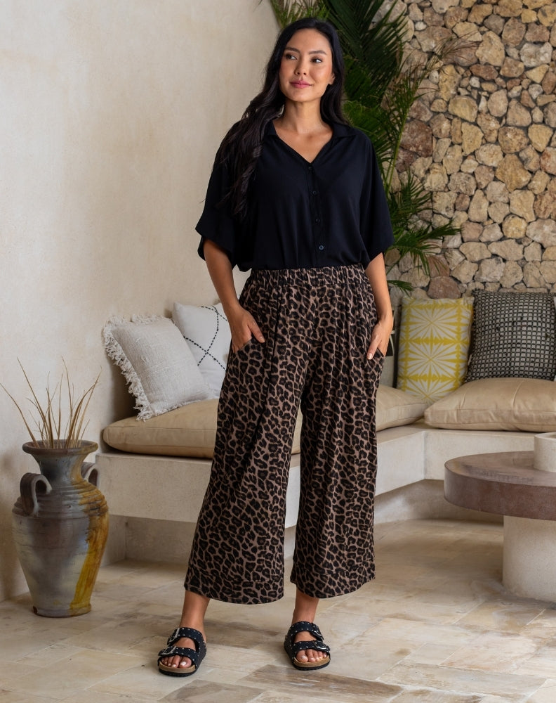 Woman wearing a black shirt and leopard print pants standing in a living room.