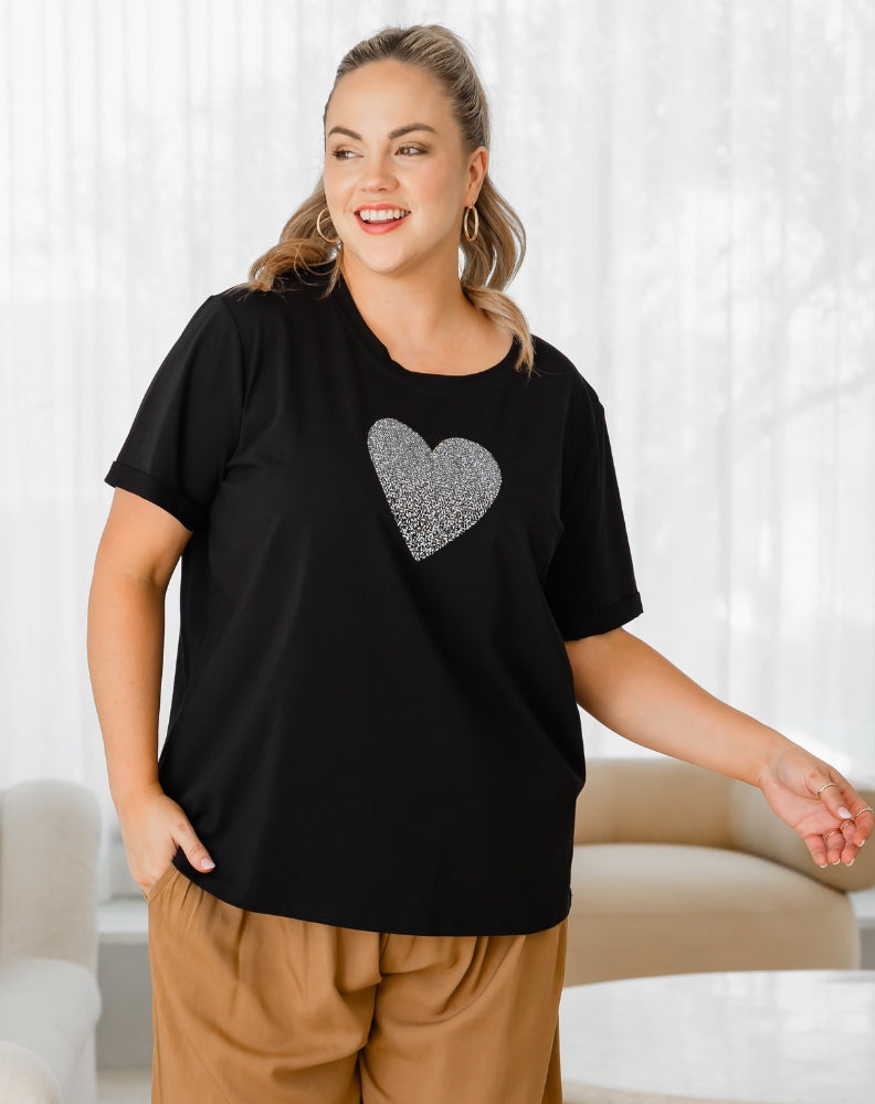 Woman wearing a black t-shirt with a silver heart design in a living room.