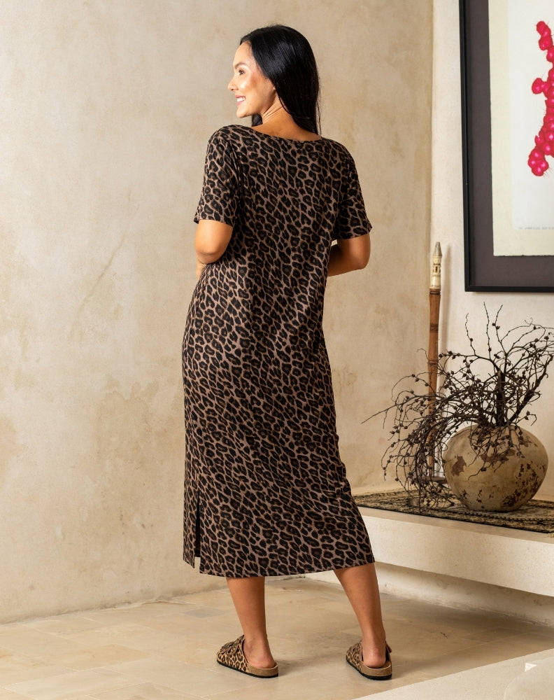 Woman wearing a leopard print dress standing in a room with a decorative vase and plant.