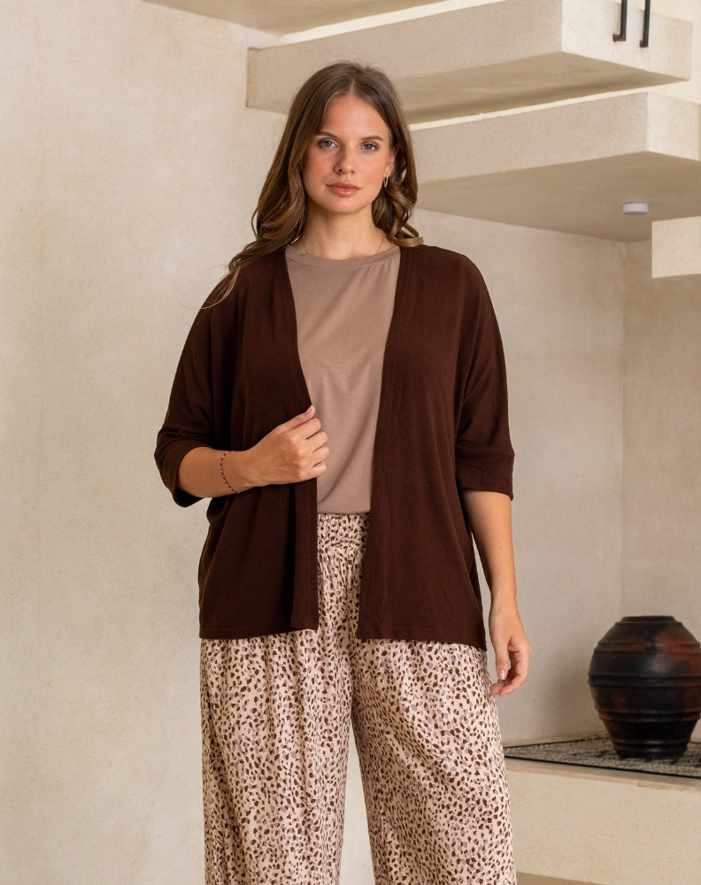 Woman wearing a brown cardigan over a beige top and leopard print pants in an indoor setting.