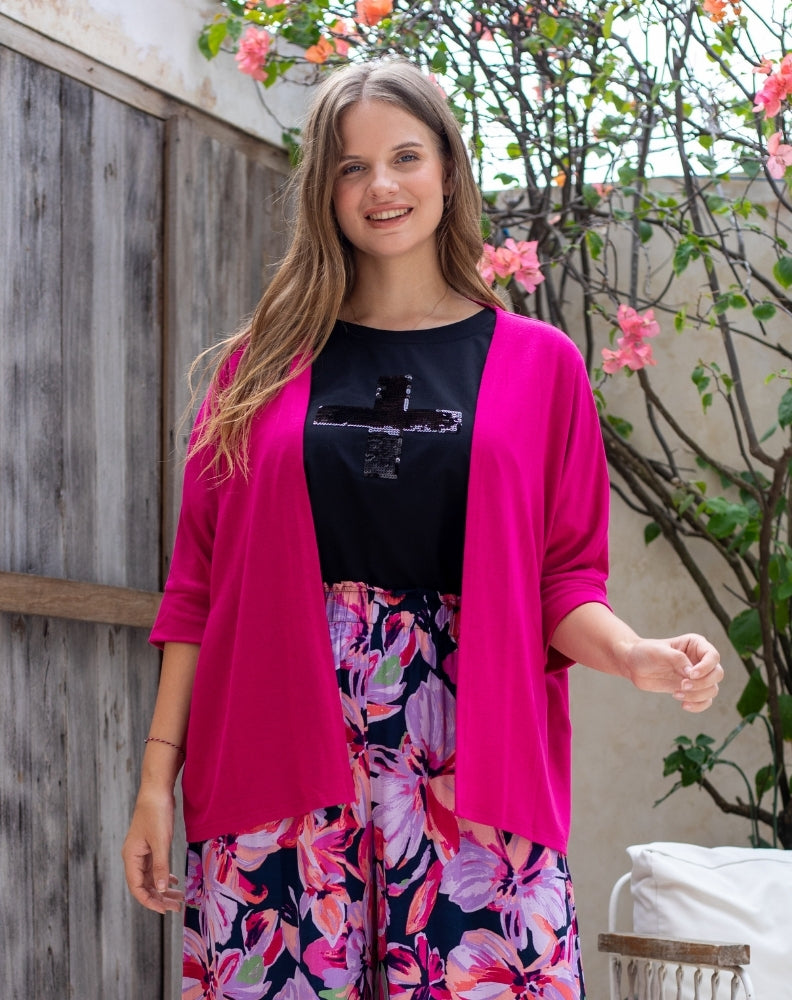 Woman wearing a bright pink cardigan over a black top and floral skirt, standing outdoors.