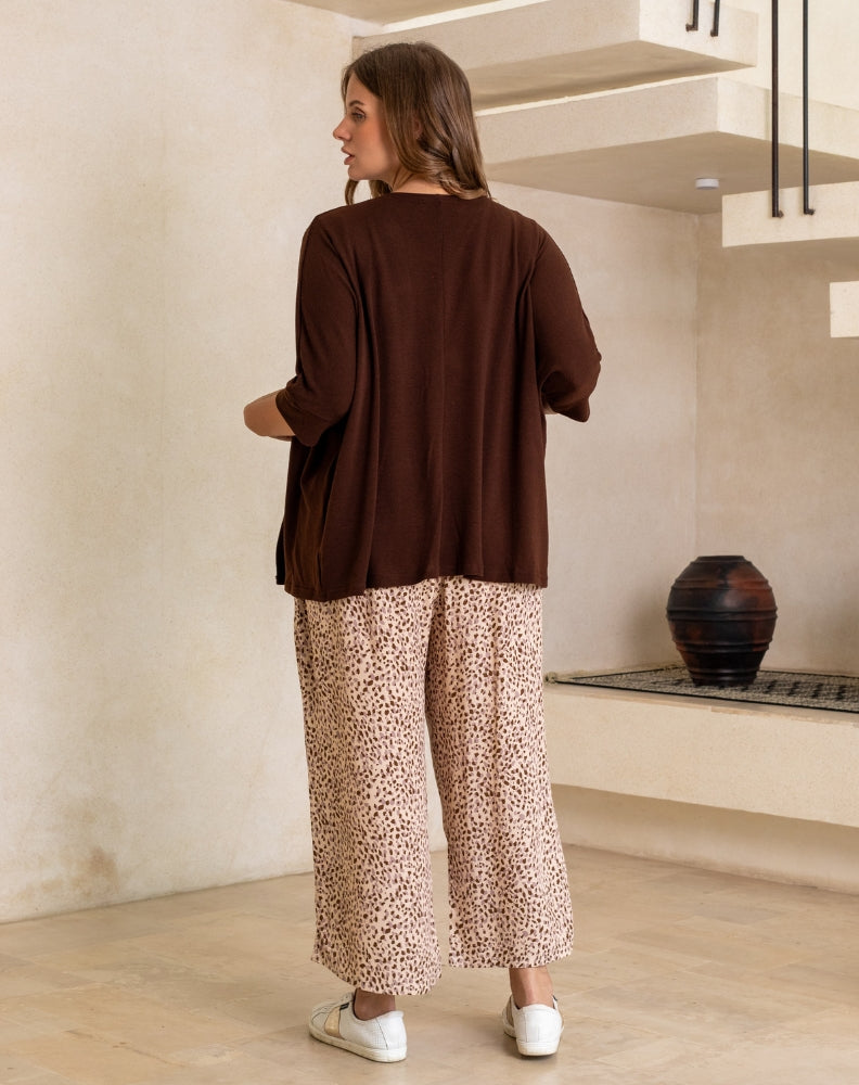 Woman wearing a brown top and patterned pants standing in a room with a neutral color scheme.