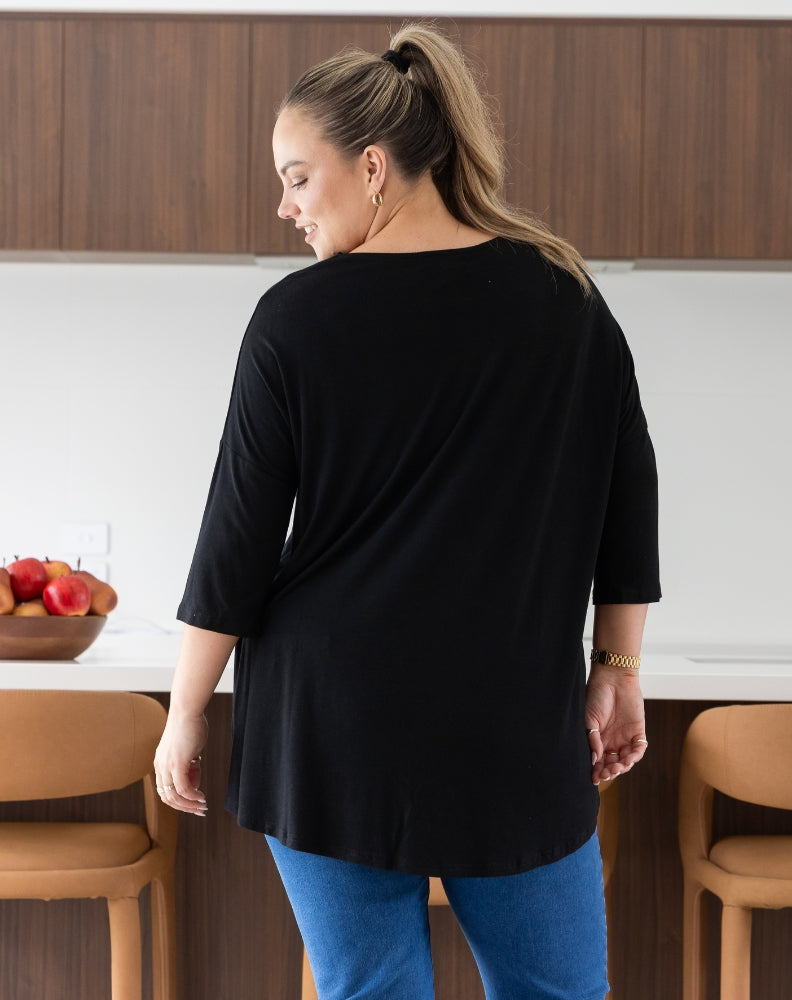 Woman wearing a black top and blue pants in a kitchen setting