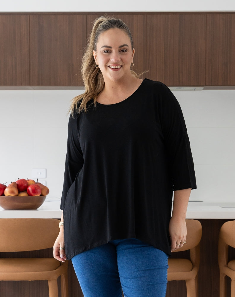 Woman in a black top and blue pants standing in a kitchen.