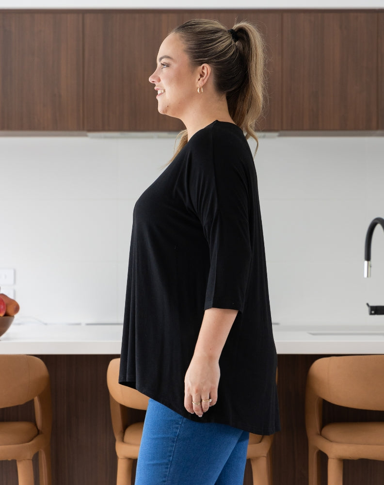Woman standing in a kitchen wearing a black top and blue jeans.