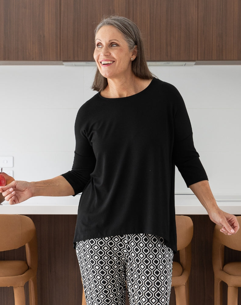 Woman in a black top and patterned pants standing in a kitchen.
