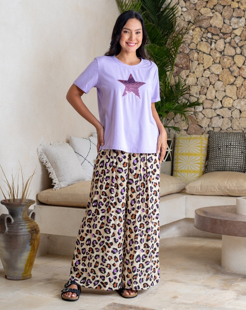 Woman wearing a light purple t-shirt with a star design and leopard print pants in a living room setting.