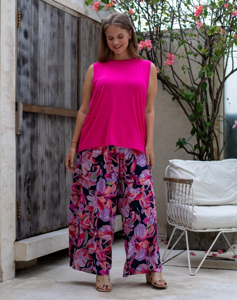 Woman wearing a bright pink top and floral pants standing in an outdoor setting.