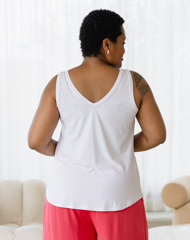 Person wearing a white tank top and pink pants in a room with a white couch and light-colored walls.