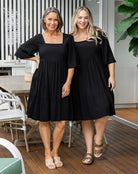 Two women wearing black dresses standing on a wooden deck.