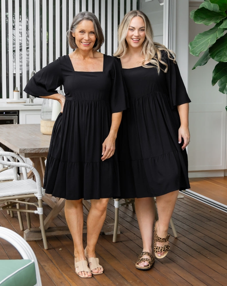 Two women wearing black dresses standing on a wooden deck.