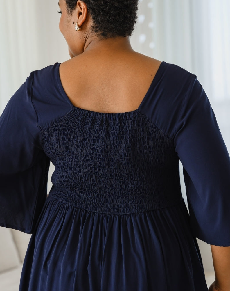 Navy blue dress with smocked bodice worn by a person, against a neutral background