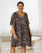 Woman wearing a leopard print dress in a bright room with white curtains.