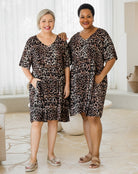 Two women wearing leopard print dresses standing in a room with white curtains.