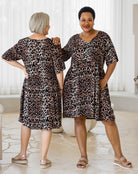 Two women wearing leopard print dresses standing in a room with white curtains.