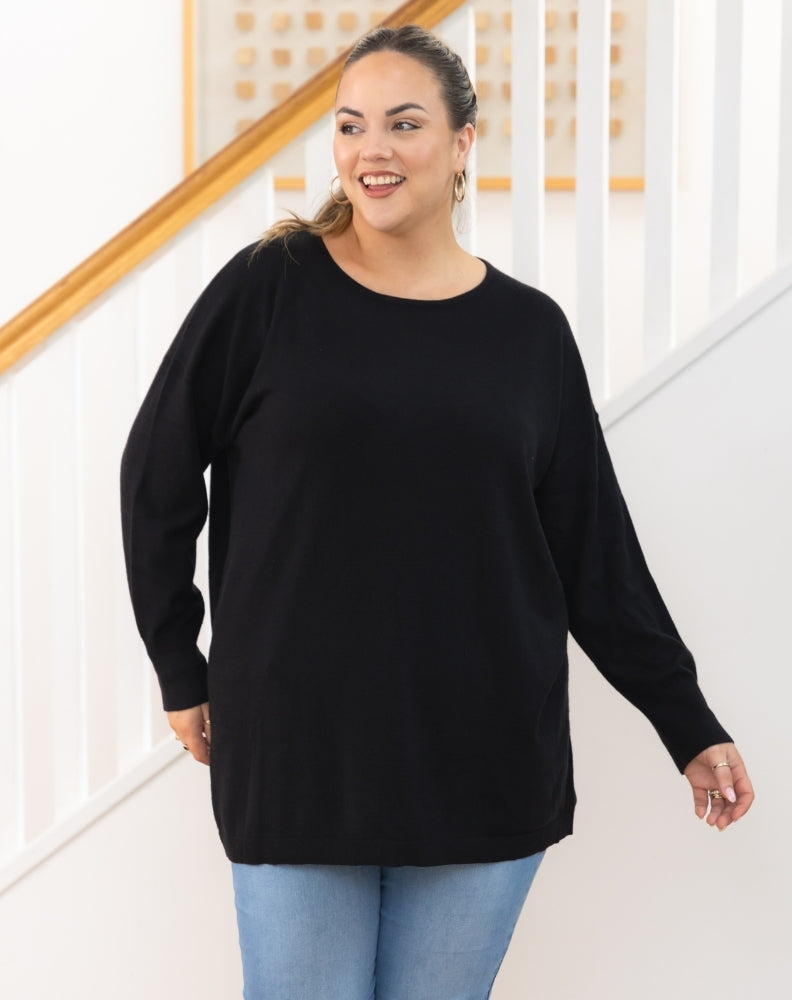 Woman wearing a black sweater and light blue jeans standing indoors.