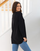 Woman wearing a black long-sleeve top and blue jeans standing in a staircase.