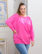 Woman wearing a bright pink sweatshirt and blue jeans indoors.