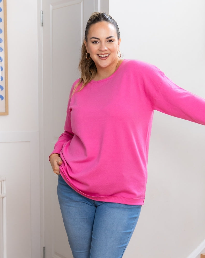 Woman wearing a bright pink sweater and blue jeans indoors.