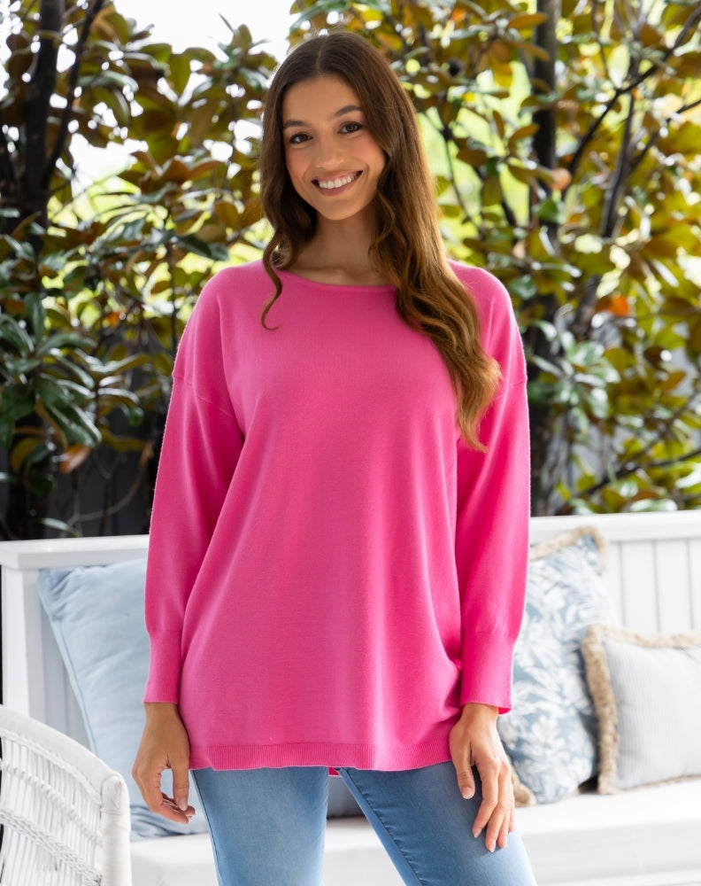 Woman wearing a pink long-sleeve top standing outdoors with greenery in the background