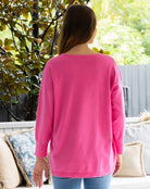 Woman wearing a pink long-sleeve shirt standing outdoors with greenery in the background