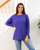 Woman wearing a purple long-sleeve top and blue jeans standing indoors.