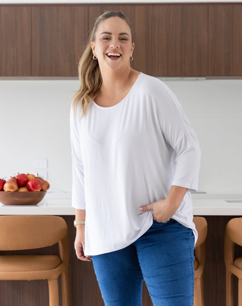 Woman in a white shirt and blue jeans standing in a kitchen.