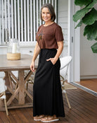 Woman in brown top and black skirt standing on a wooden deck.
