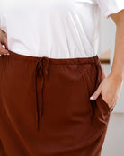 Brown pants with a drawstring waist worn by a person in a white shirt.
