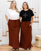 Two women standing side by side wearing brown wide-leg pants and white and black tops, smiling at the camera.