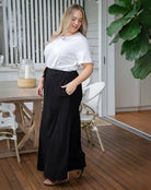 Woman in a white shirt and black skirt standing on a wooden deck.