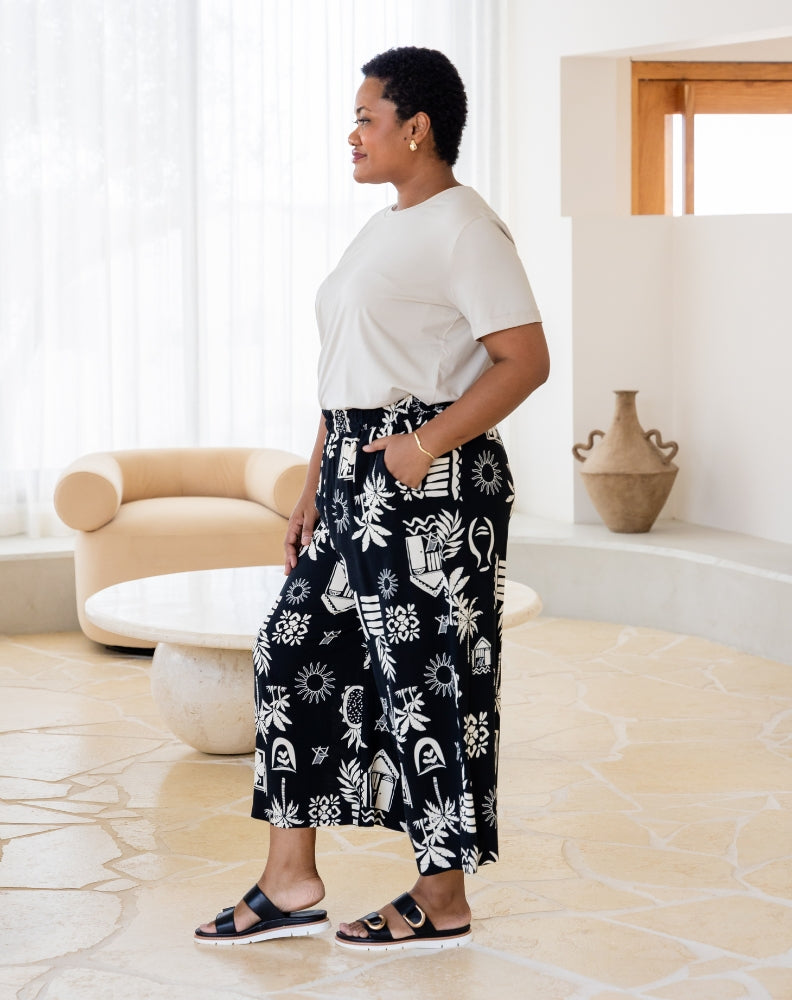 Woman wearing a white top and black patterned pants in a modern living room.