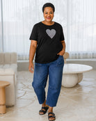 Woman wearing a black t-shirt with a heart design and blue jeans standing in a modern living room.