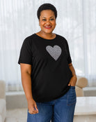 Woman wearing a black t-shirt with a silver heart design in a living room.