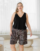 Woman wearing a black sleeveless top and leopard print shorts in a bright room.