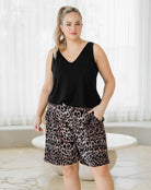 Woman wearing a black sleeveless top and leopard print shorts in a bright room.