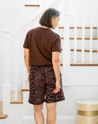 Person wearing a brown t-shirt and leopard print shorts standing in a home setting.