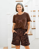 Woman wearing a brown t-shirt with a star design and leopard print shorts standing on a staircase.
