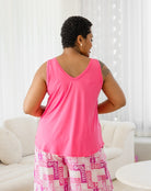 Person wearing a pink tank top and patterned pants in a bright room.