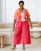 Woman wearing a colorful blouse and red pants in a living room setting