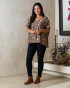 Woman wearing a leopard print top and black pants standing indoors.