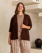 Woman wearing a brown cardigan, beige top, and leopard print pants indoors.