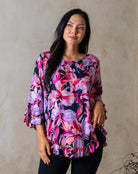 Woman wearing a colorful floral blouse against a beige wall