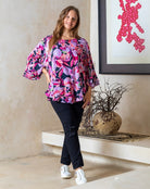 Woman wearing a colorful floral blouse in a room with a decorative plant and abstract art.