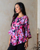 Woman wearing a colorful floral blouse against a beige wall.