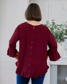 Person wearing a burgundy blouse with ruffled details in a kitchen setting