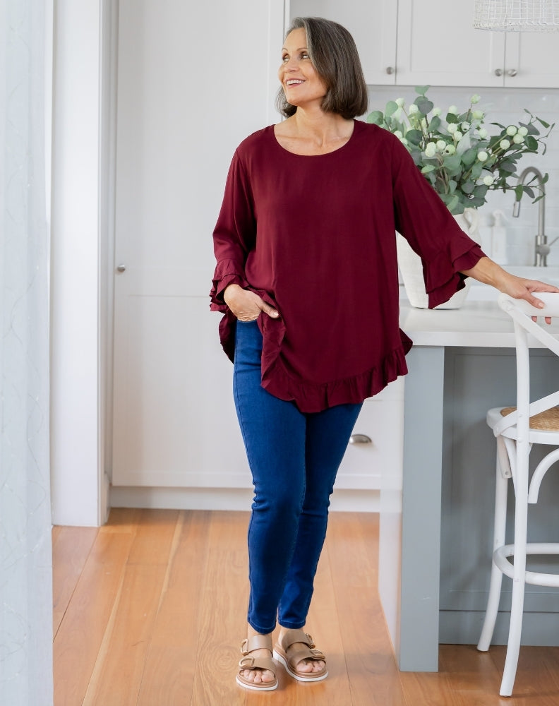 Woman wearing a burgundy top and blue jeans standing in a kitchen.