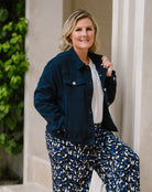 A woman posing outdoors in a dark navy blue denim jacket, a white top, and blue, white, and black patterned pants.